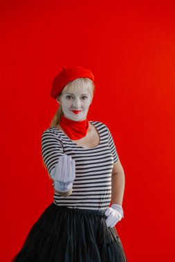 Kırmızı bereli kırmızı duvarın yanında pandomimci kadın eliyle bir işaret gösteriyor..