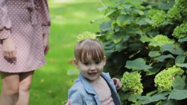 Young mother with little daughter by the bush. — Stock Video