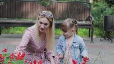 Parktaki çiçek tarhının yanında küçük kızı olan mutlu bir anne..