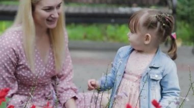 Parktaki çiçek tarhının yanında küçük kızı olan mutlu bir anne..