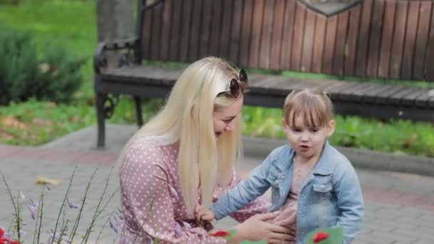 Happy young mother with little daughter near the flower bed in the park. — Stock Video