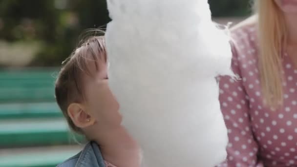 Beautiful and happy little girl eating cotton candy on the bench. Young happy mother with little girl. — Stock Video