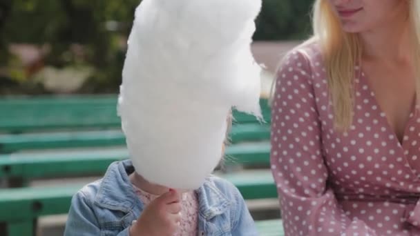 Beautiful and happy little girl eating cotton candy on the bench. Young happy mother with little girl. — Stock Video
