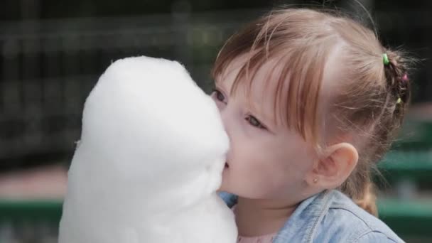 Schöne und glückliche kleine Mädchen essen Zuckerwatte auf der Bank. — Stockvideo