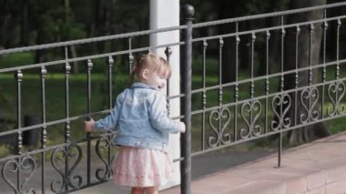 Küçük mutlu kız, korkulukların yanında yürür..