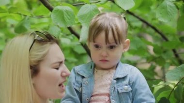 Mutlu genç anne ve küçük kızı parktaki ağacın yanında..