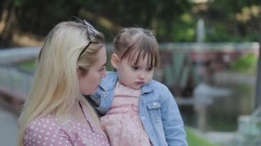 Parkta kollarında küçük kızı olan mutlu genç bir anne..