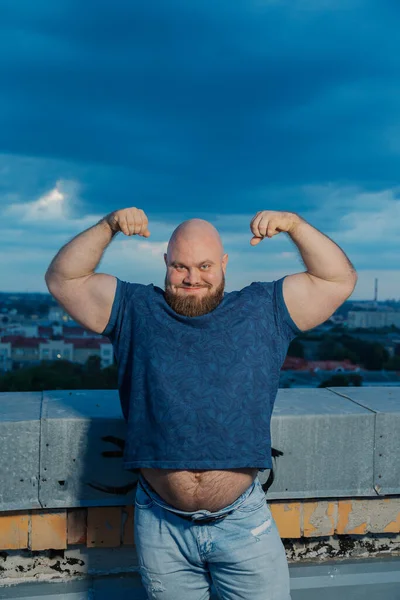Grote bebaarde bodybuilder op het dak in de avond. — Stockfoto