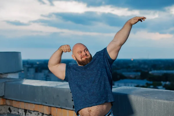 Grote bebaarde bodybuilder op het dak in de avond. — Stockfoto