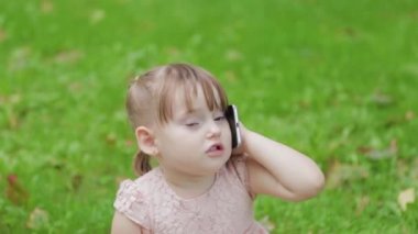 Parkta çimlerin üzerinde cep telefonuyla konuşan güzel küçük kız..