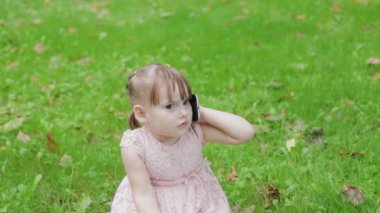 Parkta çimlerin üzerinde cep telefonuyla konuşan güzel küçük kız..