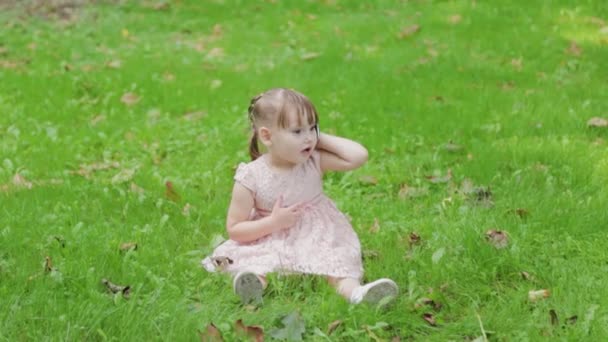 Smuk lille pige taler på en mobiltelefon i parken på græsset. – Stock-video