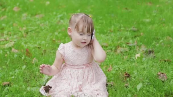 Parkta çimlerin üzerinde cep telefonuyla konuşan güzel küçük kız.. — Stok video