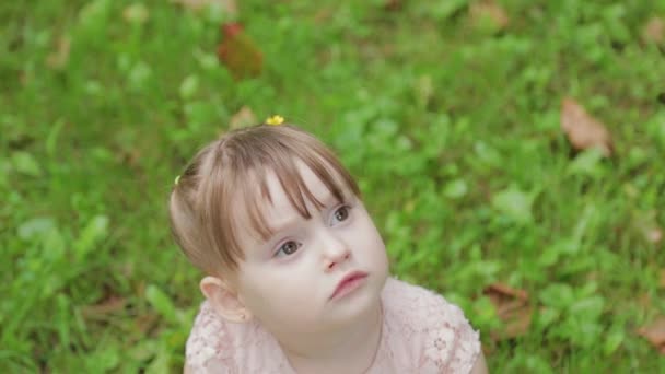 A gyönyörű kislány szomorú a fűben, aztán mosolyog.. — Stock videók