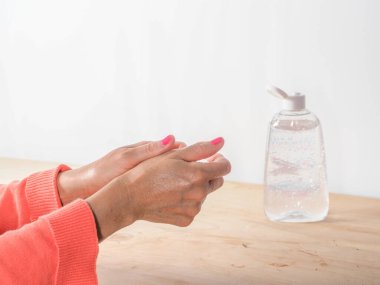 Kadın ellerini kapatırken kendini antivirüs bakteriyel jeliyle temizler ve sterilize eder. Kovid-19 'a karşı, sonbahar elbisesi, ahşap bir masanın üzerindeki turuncu renk, toprak tonları..