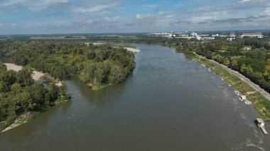 Po Nehri 'nin görkemli hava manzarası Cremona Lombardy yakınlarındaki yemyeşil manzaralar ve ağaçların arasından akıyor. Ufukta görünen uzak şehir binaları parlak mavi gökyüzünün altında bölgenin doğal güzelliğini ve kentsel büyümesini yakalıyor.