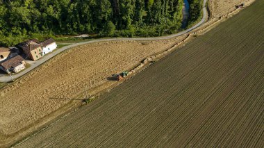 Hava perspektifi çiftçinin traktör kullandığını gösteriyor, tarlada saman kesiyor kırsal yolda gezinerek uzak ufka doğru uzanıyor.