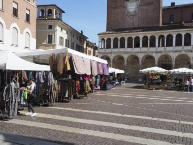 Cremona, İtalya - 3 Eylül 2025 Vibrant açık-hava pazar tezgahları Cremona Lombardy İtalya 'nın tarihi şehir merkezinde mavi altında güneşli bir günde renkli tekstil ve giysiler sergileniyor