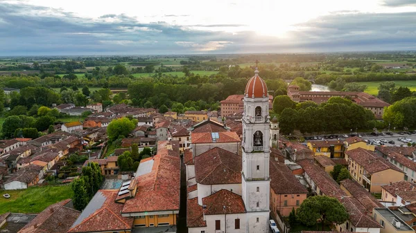 Hava manzarası Pontevico 'yu çekiyor, büyüleyici bir Brescia kasabası, önde gelen bir kilise kulesi, terracotta çatıları, yemyeşil ve gün batımında sakin Oglio Nehri.