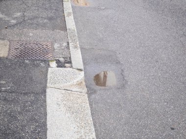 Kaldırımlı ve Kanalizasyon Izgarası Detaylı Su birikintisi ve desenli Yüzeyi Gösteren Islak Asfalt Alanı Görüntüsünü Kapat