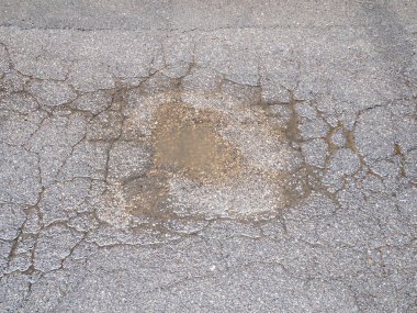 Çatlak asfaltın soyut dokulu arka planını granüler toprak ve yüzeydeki kusurları ortaya çıkaran küçük taşlarla kapat ve aşınma şekilleri hafif bir sıkıntı yaratıyor.