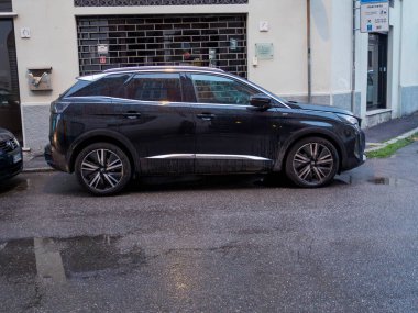 Cremona, İtalya 26 Ağustos 2025 Black Peugeot 3008 parkedilmiş sokak kenarı, yağmurdan sonra ıslak asfalta yansıyor, yan profil su birikintisinin aynasında yüzey gibi parıldıyor.