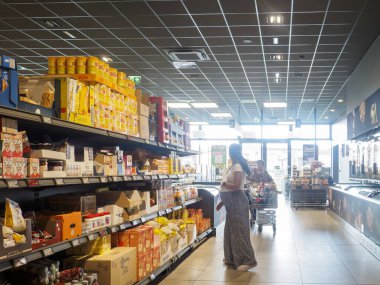 Cremona, İtalya - 11 Eylül 2025 Uzun desenli etekli genç bir kadın İtalyan indirimli bir süpermarkette çeşitli ürünlerle dolu raflardan sebze seçiyor.