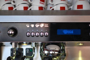 Cremona, İtalya 19 Temmuz 2025 Profesyonel Wega Polaris espresso makinesi dijital logo sergiliyor, yanında beyaz bardaklar yığılı, geleneksel İtalyan Musetti Kafe 'sinde zengin espresso demliyor.