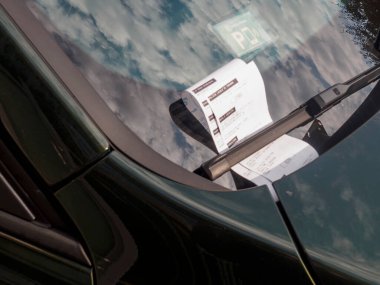 Cremona, İtalya 16 Eylül 2025 Koyu yeşil bir Opel Astra 2009 ön camında sileceklerin altında park cezası. Gökyüzündeki bulutları yansıtıyor.