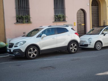 Cremona, İtalya 16 Eylül 2025 Beyaz Opel Mokka - 2012 serisi - kompakt SUV ve Fiat 500 - 2007 mevcut serisi - İtalya 'da dar bir sokağa park edilmiş şehir arabası, kentsel yaşam ve ulaşım