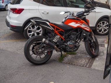 Cremona, İtalya 16 Eylül 2025 KTM 125 Duke motosikleti. Turuncu ve siyah çıplak bir spor bisikleti. Şehir caddesinde beyaz bir SEAT Arona ve açık mavi bir Fiat Punto 'nun yanına park etmiş. Kentsel str gösteriliyor