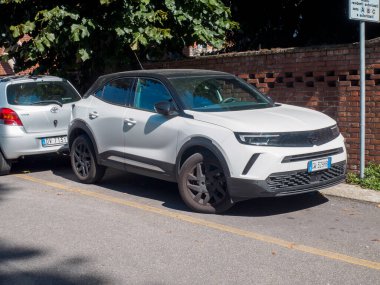 Cremona, İtalya 16 Eylül 2025 Opel Mokka B elektrikli SUV siyah çatılı tuğla duvar ve yeşilliğin yanında bir şehir sokağına park edilmiş