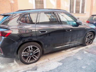 Cremona, İtalya 16 Eylül 2025 BMW X1 U11 sDrive18d - 2023 - bir şehir caddesinde park edilmiş siyah safir metalik SUv. Pencerelerine ve kaportasına tarihi yapılar yansıtıyor.