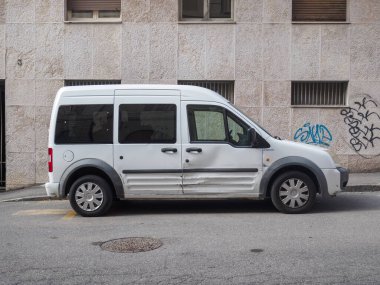 Cremona, İtalya 16 Eylül 2025 Ford Transit Connect minibüsü, ilk nesil beyaz 2002 model, yan paneli çökmüş, duvar yazıları olan bir binanın yakınındaki bir şehir sokağına park edilmiş.