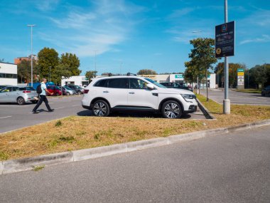 Cremona, İtalya 16 Eylül 2025 Renault Koleos 2022 beyaz SUV gündüz vakti bir Aldi süpermarketinin otoparkına park edilmiş, yanından geçen bir adam, arka planda görünen iletişim kulesi,