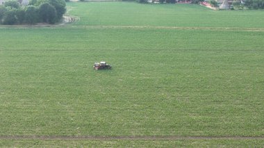 İtalya 'nın tarihi kenti Piacenza yakınlarındaki uçsuz bucaksız yeşil soya tarlasında tarım ürünlerini uygulayan bir traktörü kullanan bir çiftçinin hava perspektifi yenilikçi bir görünüm sergiliyor.