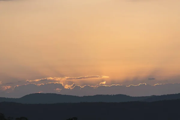 Sunset over the Sunshine Coast hinterland.  We watch as the sun disappears behind the clouds, it\'s golden rays set fire to the fragile edges of the clouds.