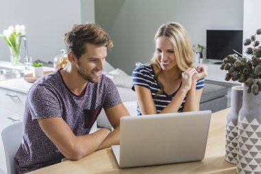 An attractive young happy couple on a laptop in a stylish modern apartment. clipart