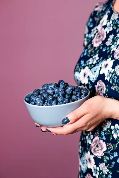 女性手的特写镜头 盛满新鲜蓝莓的碗 穿着华丽蓝色礼服的妇女站在紫色背景前 — 图库照片