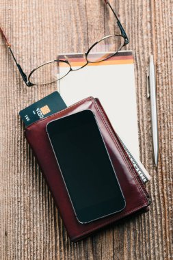 Smartphone ile boş ekran, cüzdan, Doları banknot, banka kredi kartları ve ahşap masa üstünde defter. Yukarıdan görüntüleyin. Dikey yazdırma yönü