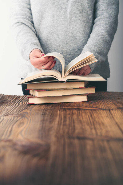 Young woman turning pages of old book on wooden table in antique bookstore. Woman wearing grey sweater and jeans. Vertical photo. Space for text