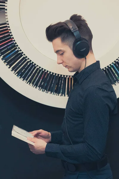 Νεαρός Άνδρας Ακούει Μουσική Μέσω Των Ακουστικών Στέκεται Δίπλα Ράφι — Φωτογραφία Αρχείου