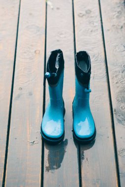Mavi wellies yağmur sırasında ahşap sundurma duran