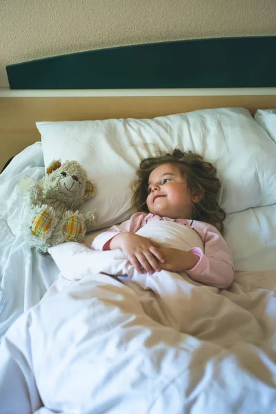 Маленькая девочка, лежащая утром в постели с плюшевым мишкой — стоковое фото