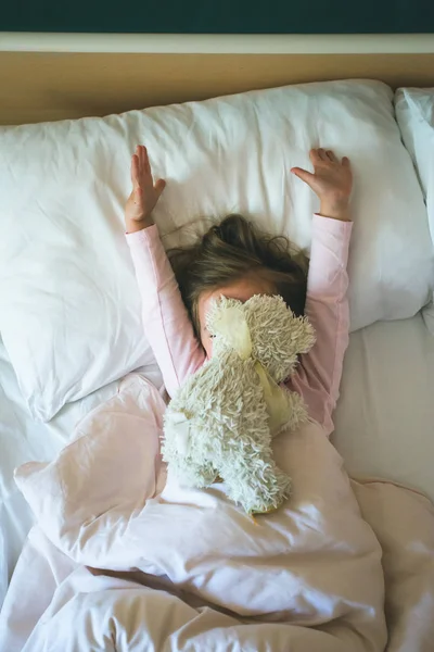 Niña acostada en una cama con osito de peluche por la mañana — Foto de Stock