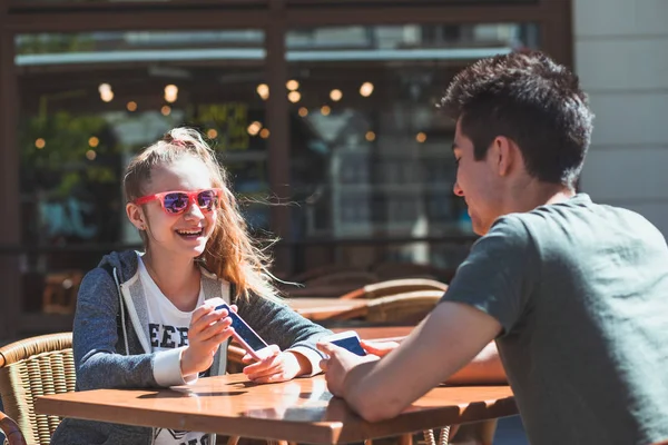 Молодая женщина и мужчина сидят в тротуаре кафе говорить и использовать м — стоковое фото