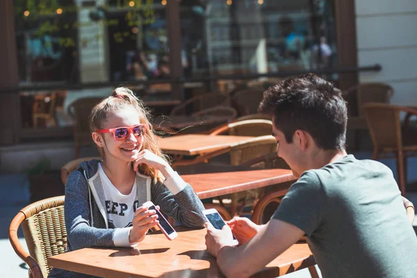 Młoda kobieta i mężczyzna siedzi w kawiarni chodniku rozmawiając i używając m — Zdjęcie stockowe