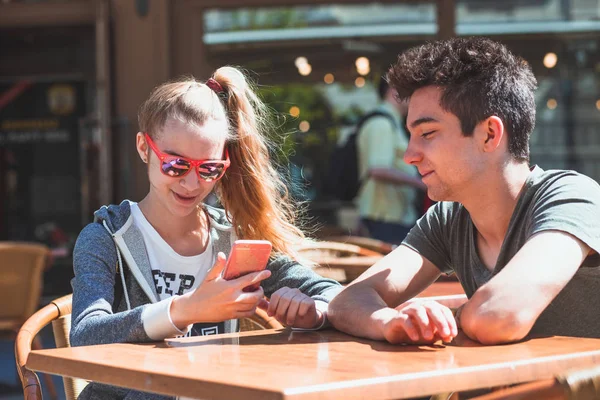Молодая женщина и мужчина сидят в тротуаре кафе говорить и использовать м — стоковое фото
