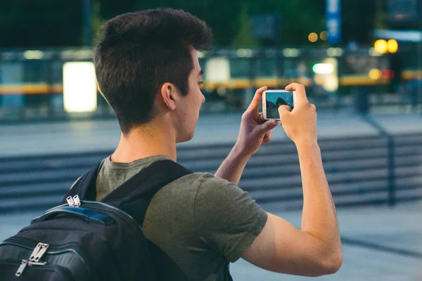 Молодой человек с рюкзаком фотографирует со смартфона — стоковое фото