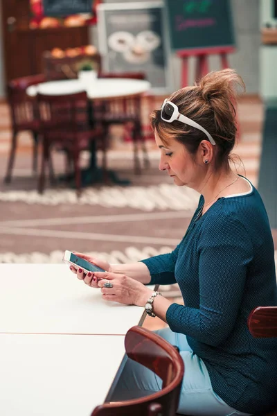 Młoda kobieta za pomocą telefonu komórkowego siedzi przy stole w kawiarni — Zdjęcie stockowe